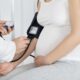 Close-up Of Male Doctor Measuring Blood Pressure Of Pregnant Woman In Clinic